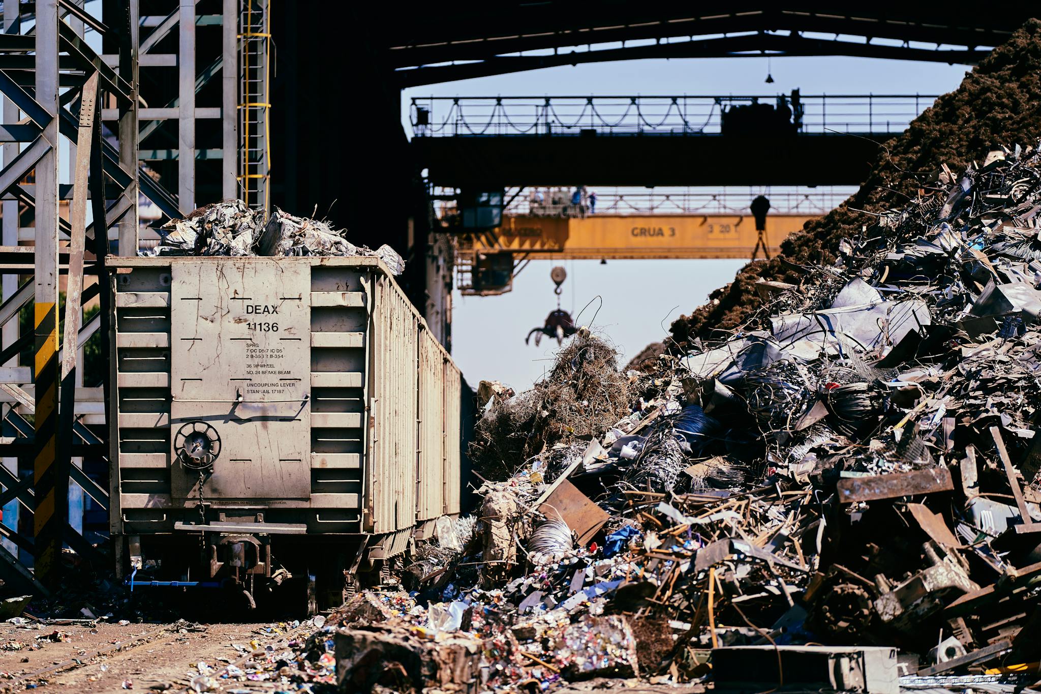 A dynamic industrial scene featuring a scrap yard with a train car and crane lifting debris.